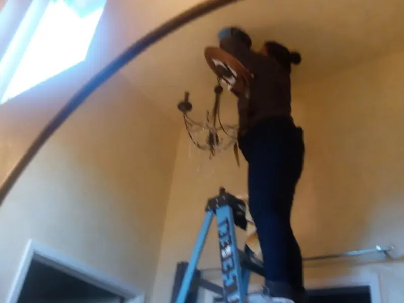Electrician installing a chandelier in a Gaines residence